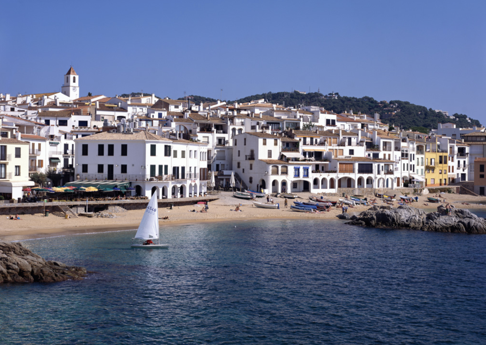 Le village de Calella de Palafrugell vu depuis la mer, maisons blanches et voilier