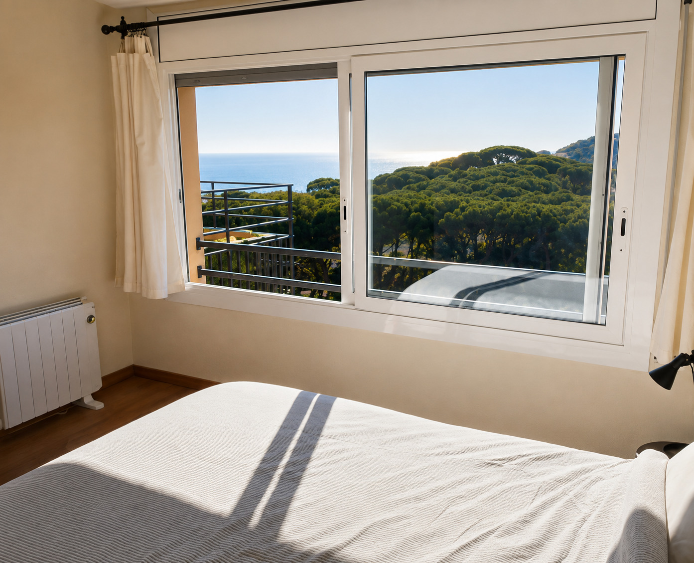Chambre principale avec grand lit et fenêtre donnant sur les pins et la mer